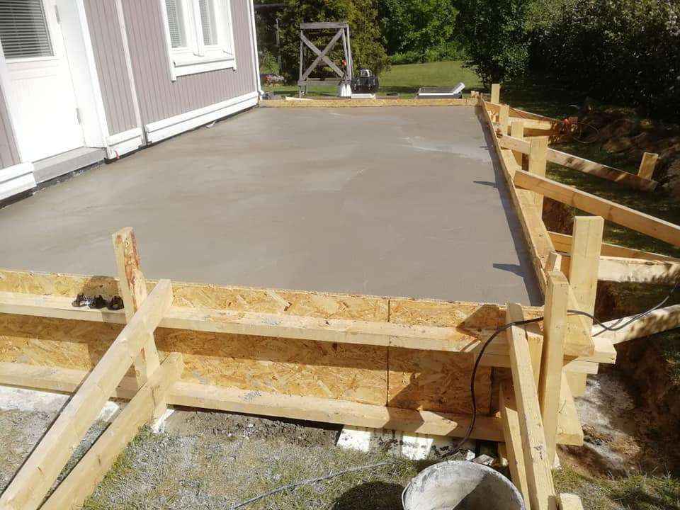 Tuore betonilaatta on valettu puisten muottien sisään, ulkona valoisa sää.