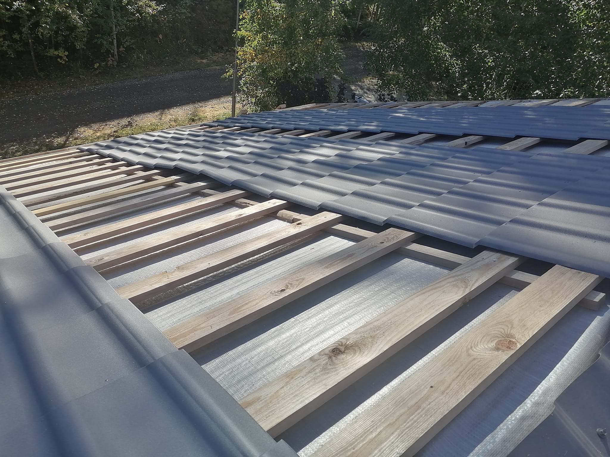 Katto on rakenteilla, puurimoja ja harmaita kattotiiliä näkyy. Valoisa sää.