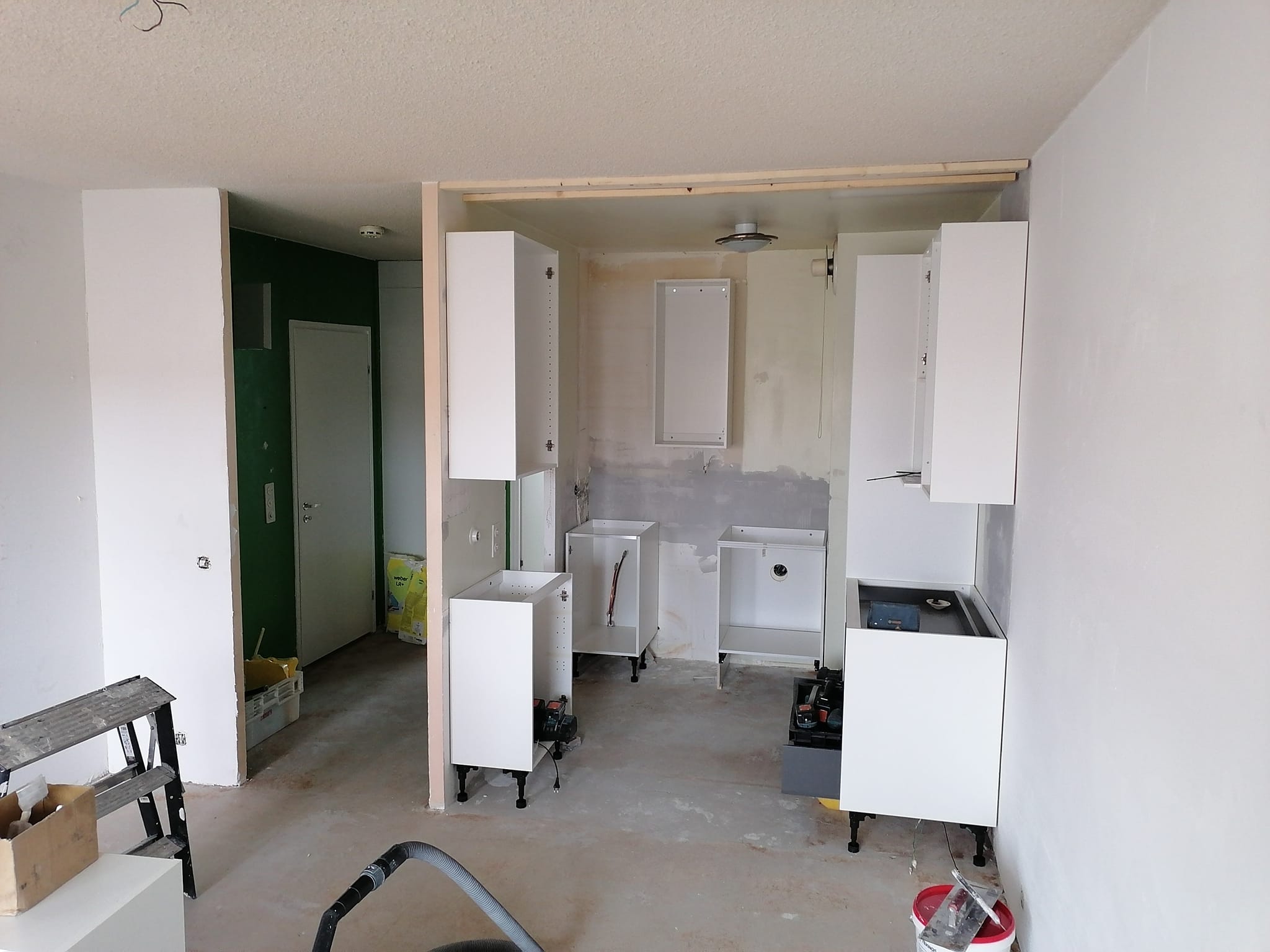 Keskeneräinen keittiö valkoisilla kaapeilla, puurungolla ja työkalut lattialla, valaistus on kirkas.