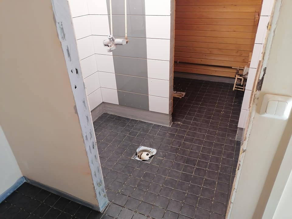 Kylpyhuoneen sisätila, jossa on harmaat laatat, puinen sauna ja valkoinen valokytkin.