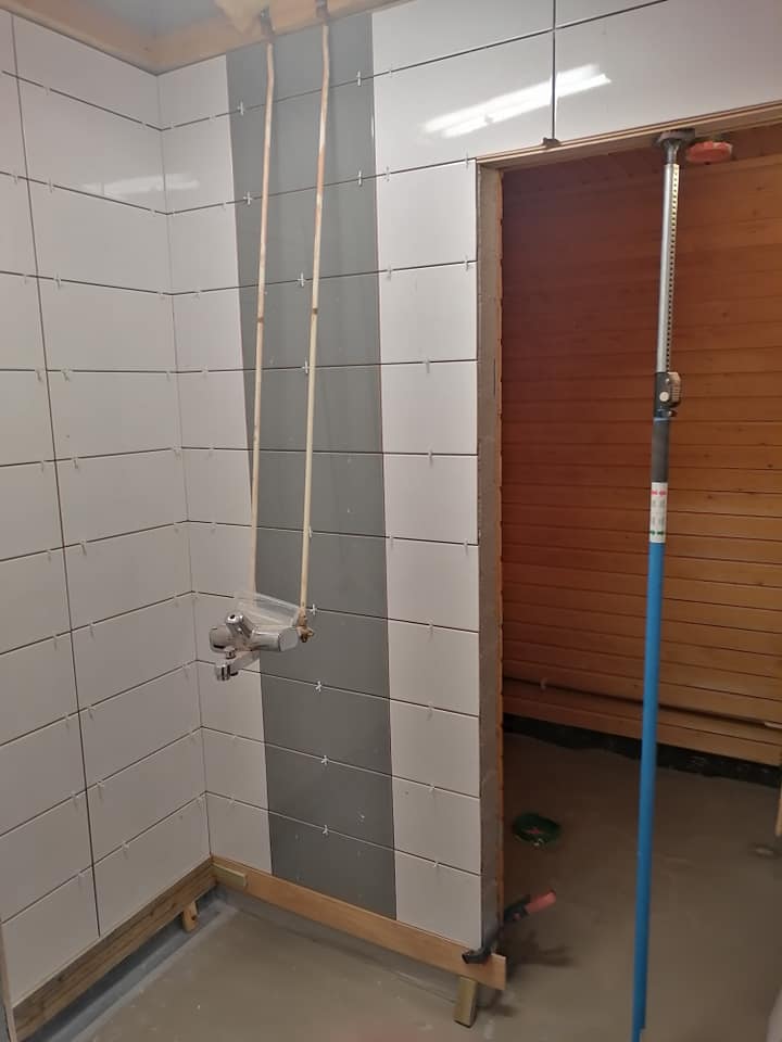 Kylpyhuoneen seinät on laatoitettu valkoisilla ja harmailla laatoilla, ja seinässä on kiinni suihkun hana.