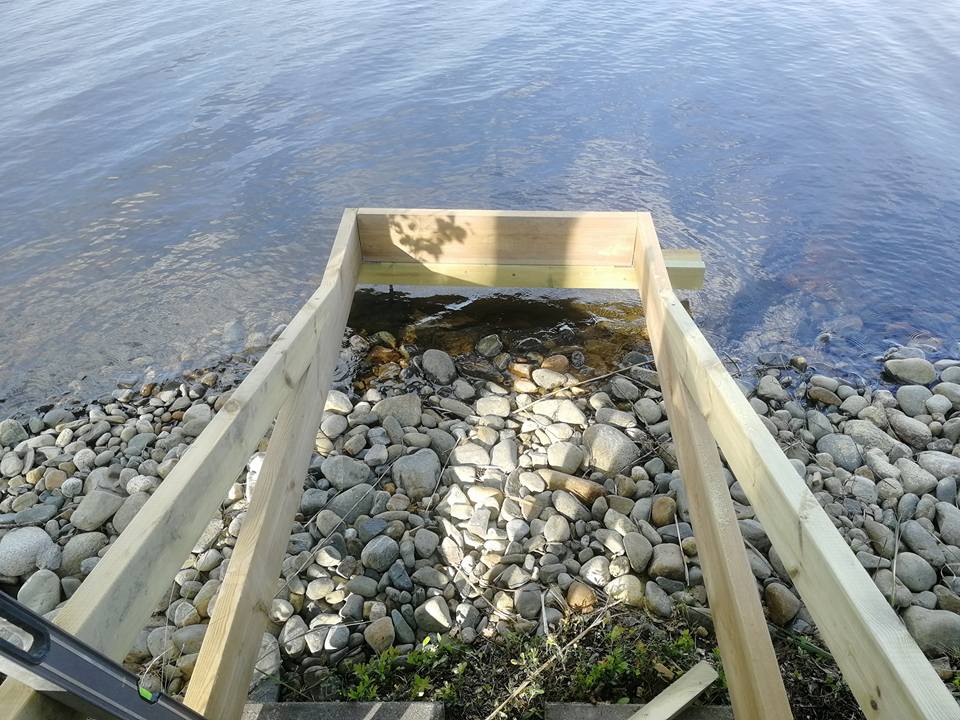 Rakenteilla oleva puinen laituri kivikkoisella rannalla, veden äärellä, valoisassa säässä.