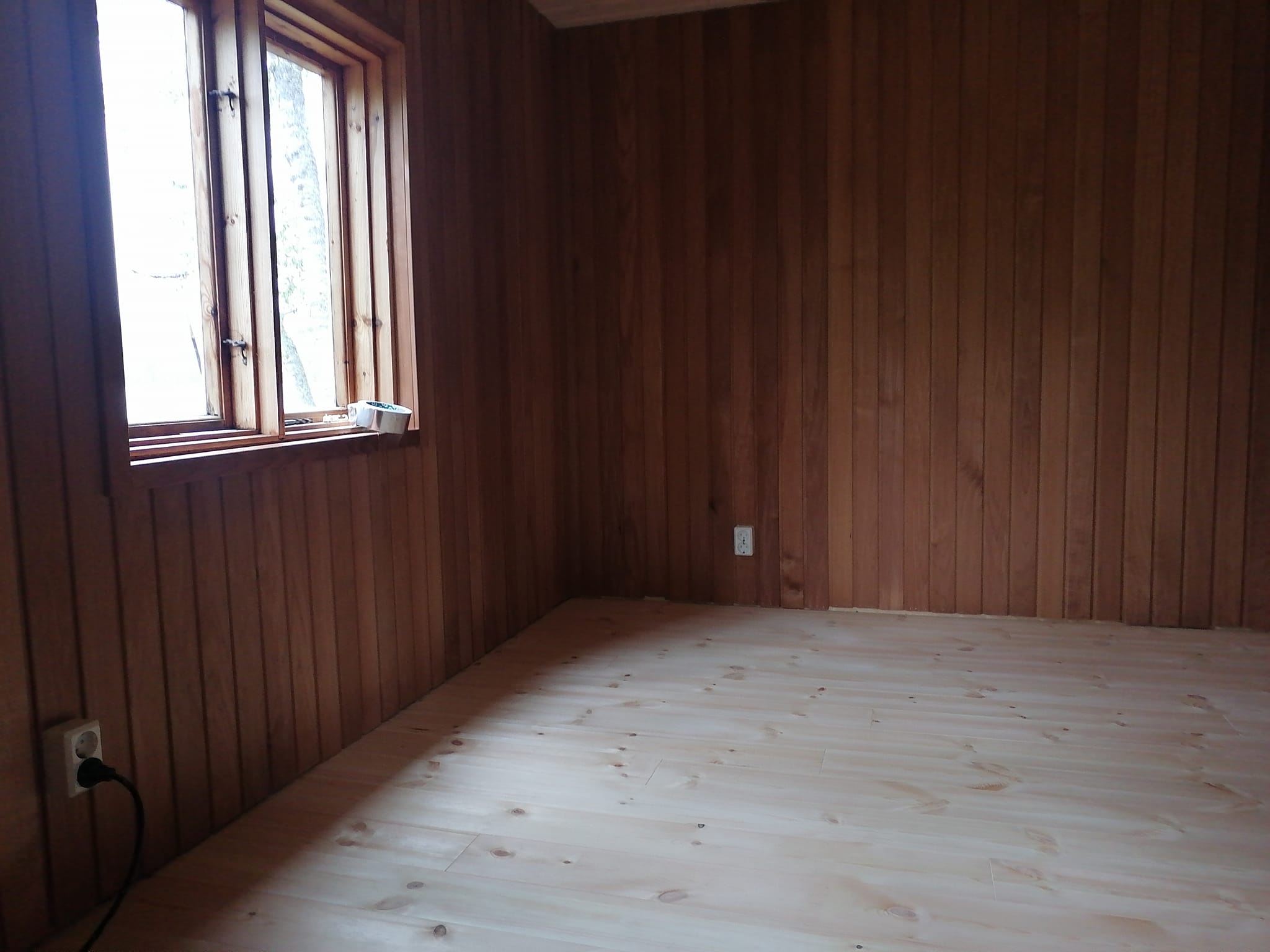 Huoneessa on puupaneliseinät, vaalea puulattia ja avoin ikkuna.