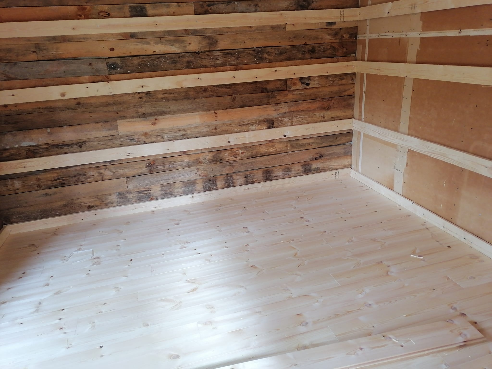 Huoneessa on puulattia, toinen seinä on tummaa puuta ja toinen vaaleaa levyä puurimoilla.