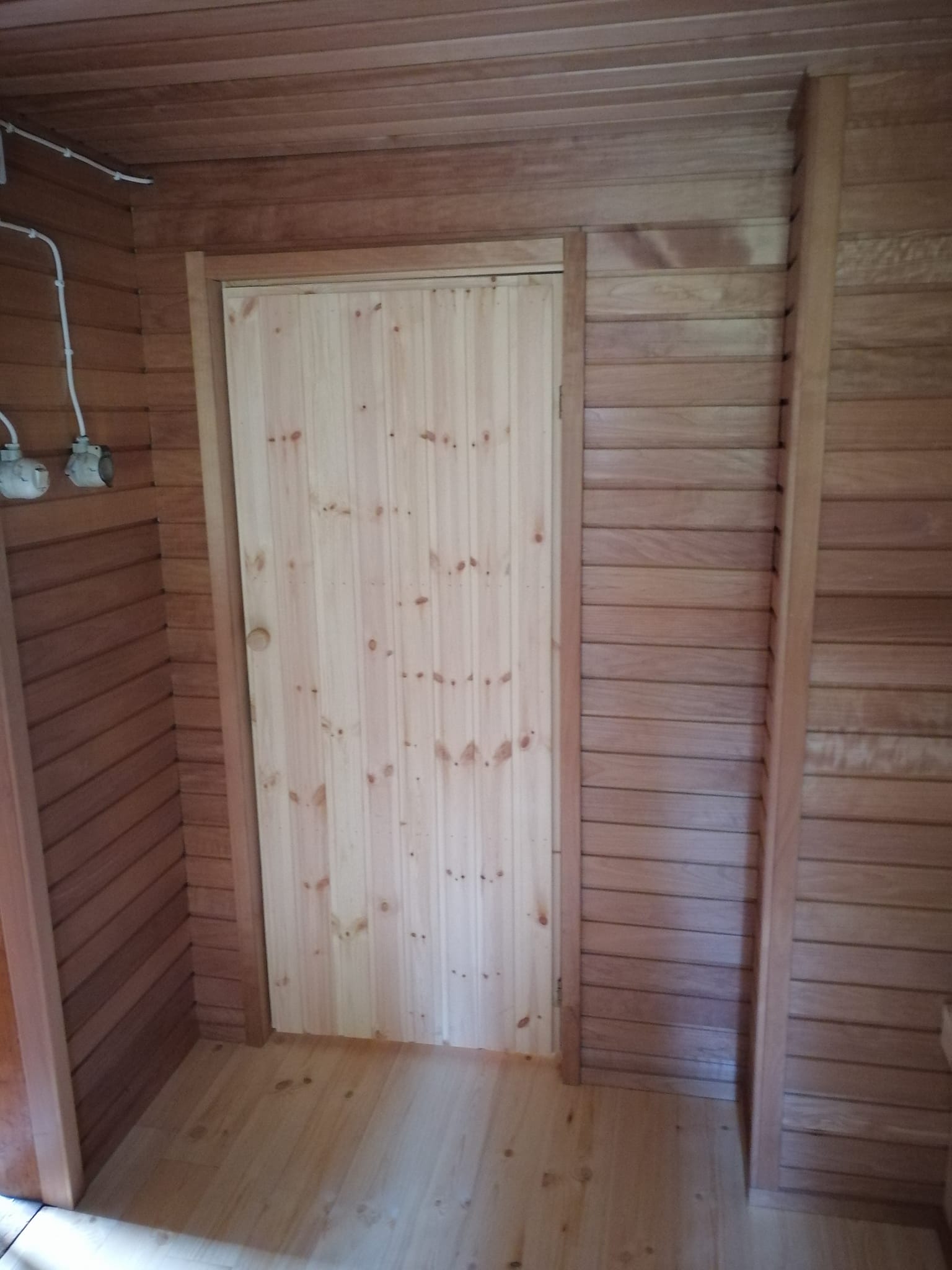 Puinen huone, jossa on puinen ovi, puulattia ja puupaneeliseinät. Valoisa ja lämmin tunnelma.