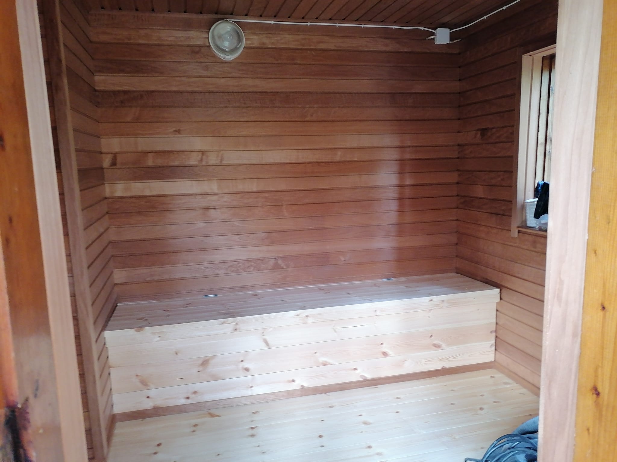Puupaneloitu huone, jossa on penkki ja valaisin katossa.
