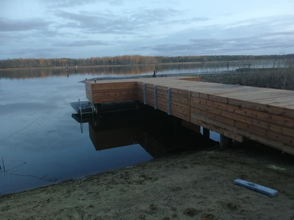 Puinen laituri ulottuu tyynelle järvelle, taustalla metsä ja pilvinen taivas.