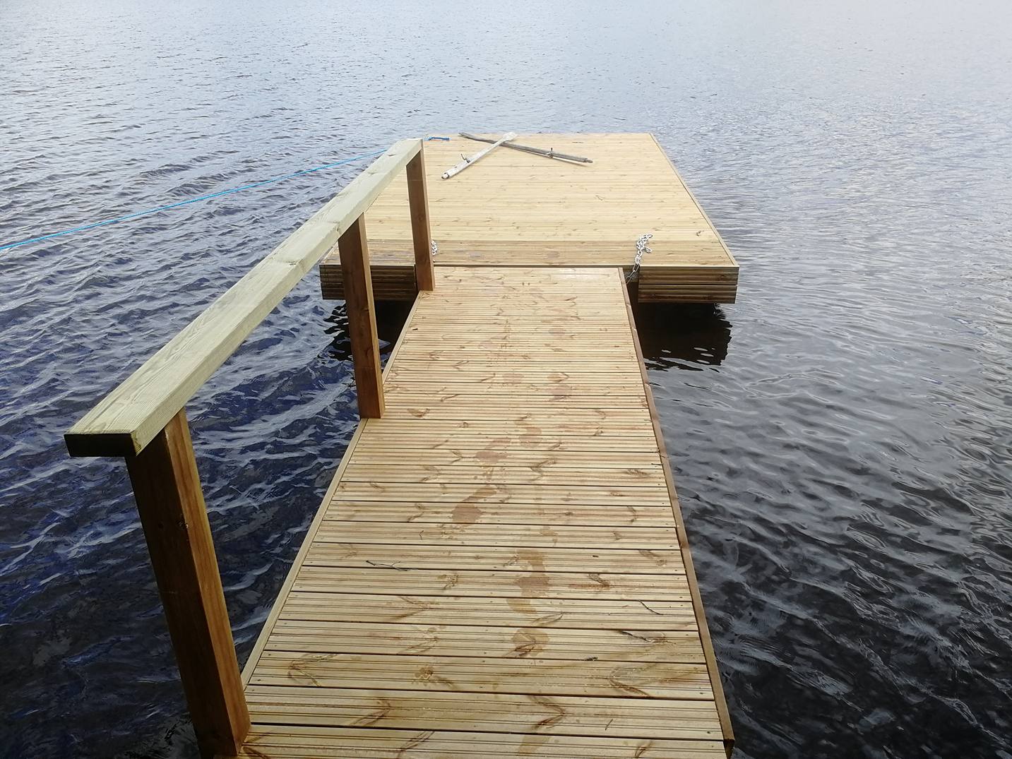 Puinen laituri järvellä, jossa on kaide ja kelluva taso, valoisa ja luonnonläheinen.