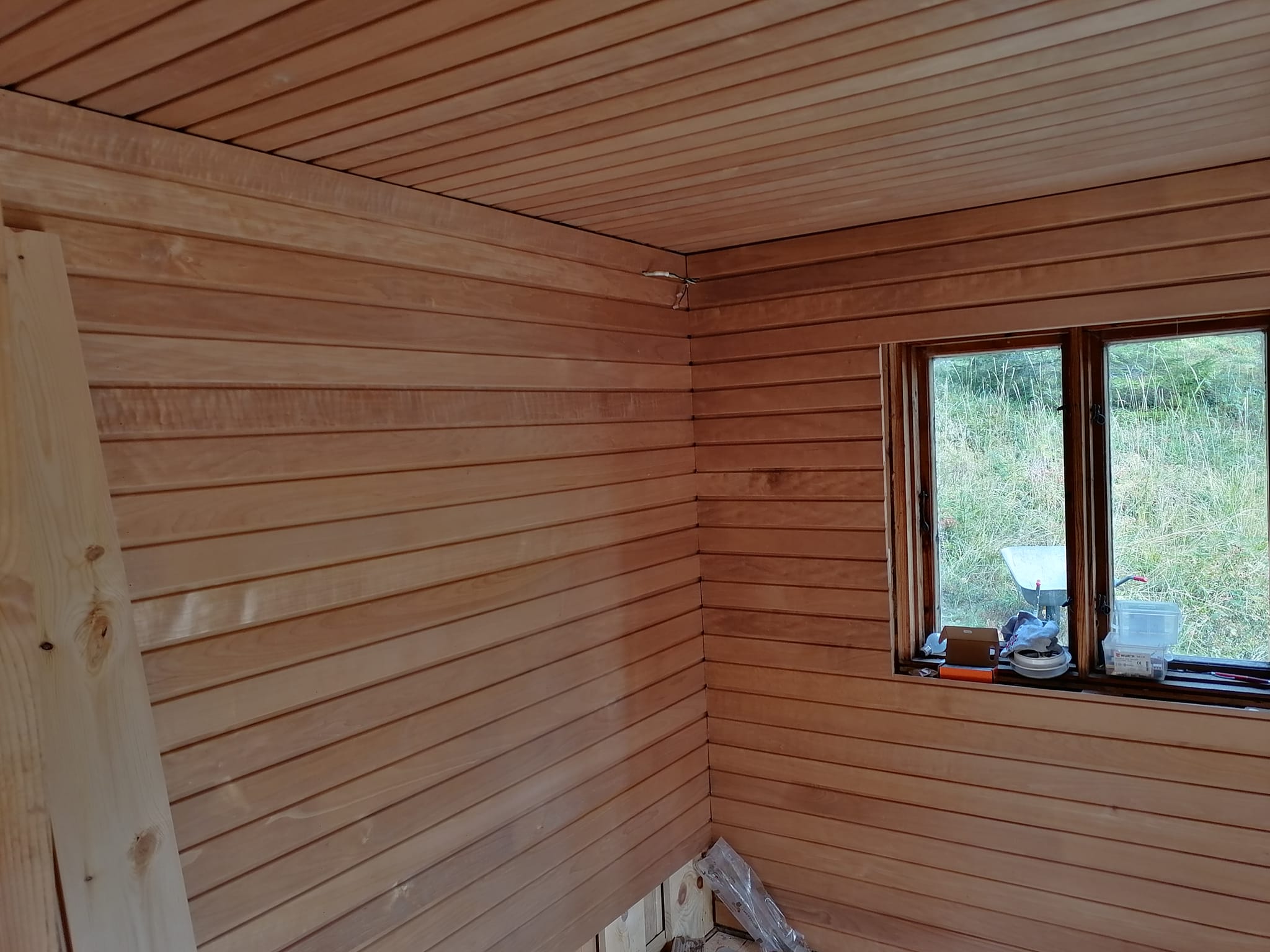 Puupaneloitu huone, jossa ikkuna ja rakennustarvikkeita.