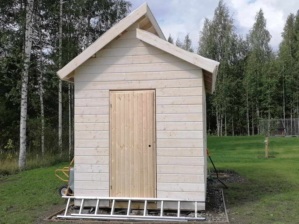 Vaalea puuvaja seisoo nurmikolla, taustalla koivuja ja havupuita, edessä alumiinitikkaat.