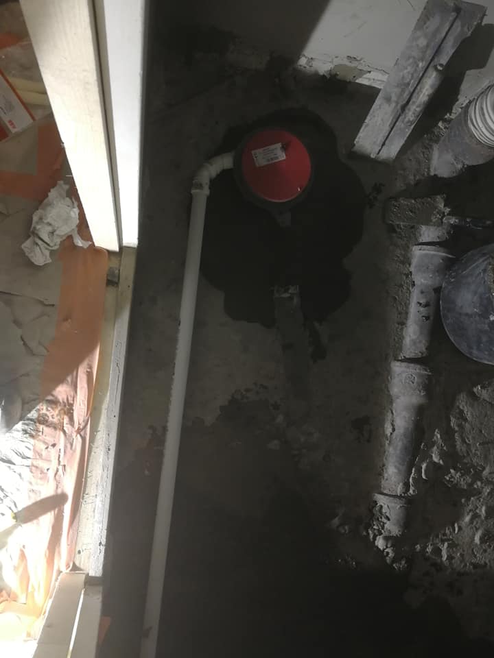 Valokuva näyttää rakennustyömaalta, jossa on näkyvissä putkia, punainen kansi ja rakennusmateriaaleja. Valo on himmeää ja epätasaista.