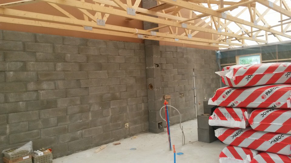 Sisätila, jossa on harmaa betoniharkkoseinä, puinen kattorakenne ja pino PAROC-eristepaketteja. Valoisa, rakennustyömaa.