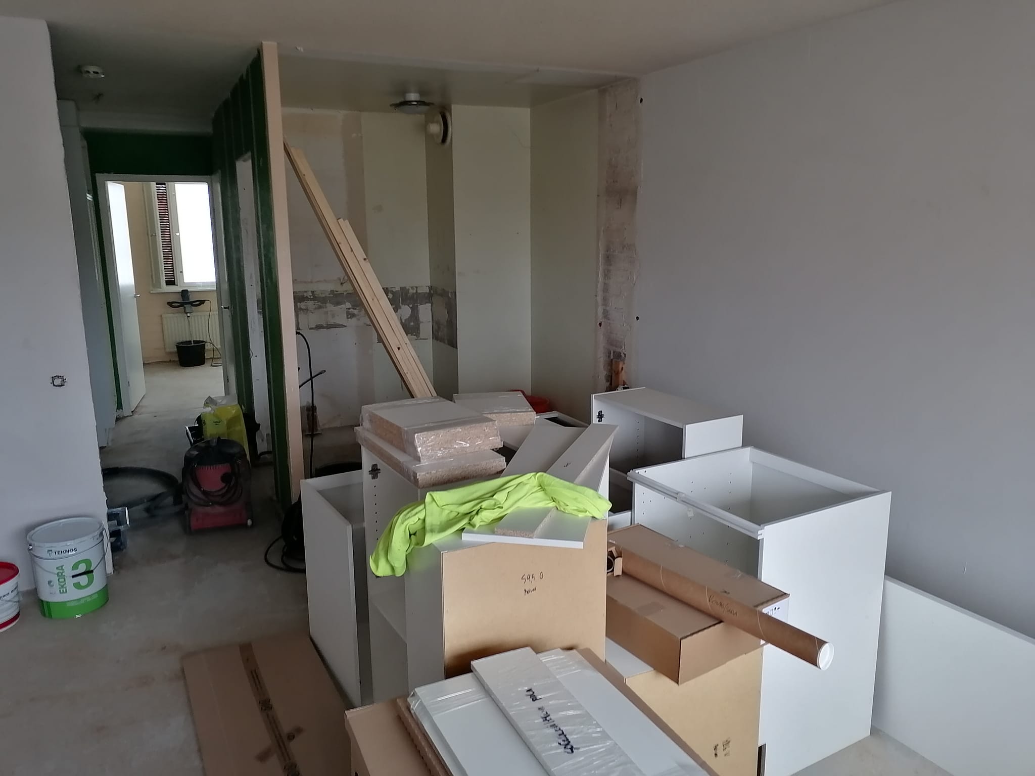 Huone remontin keskellä, jossa on valkoisia kaappeja, maalitölkkejä ja työkaluja, valaistus on luonnollinen.