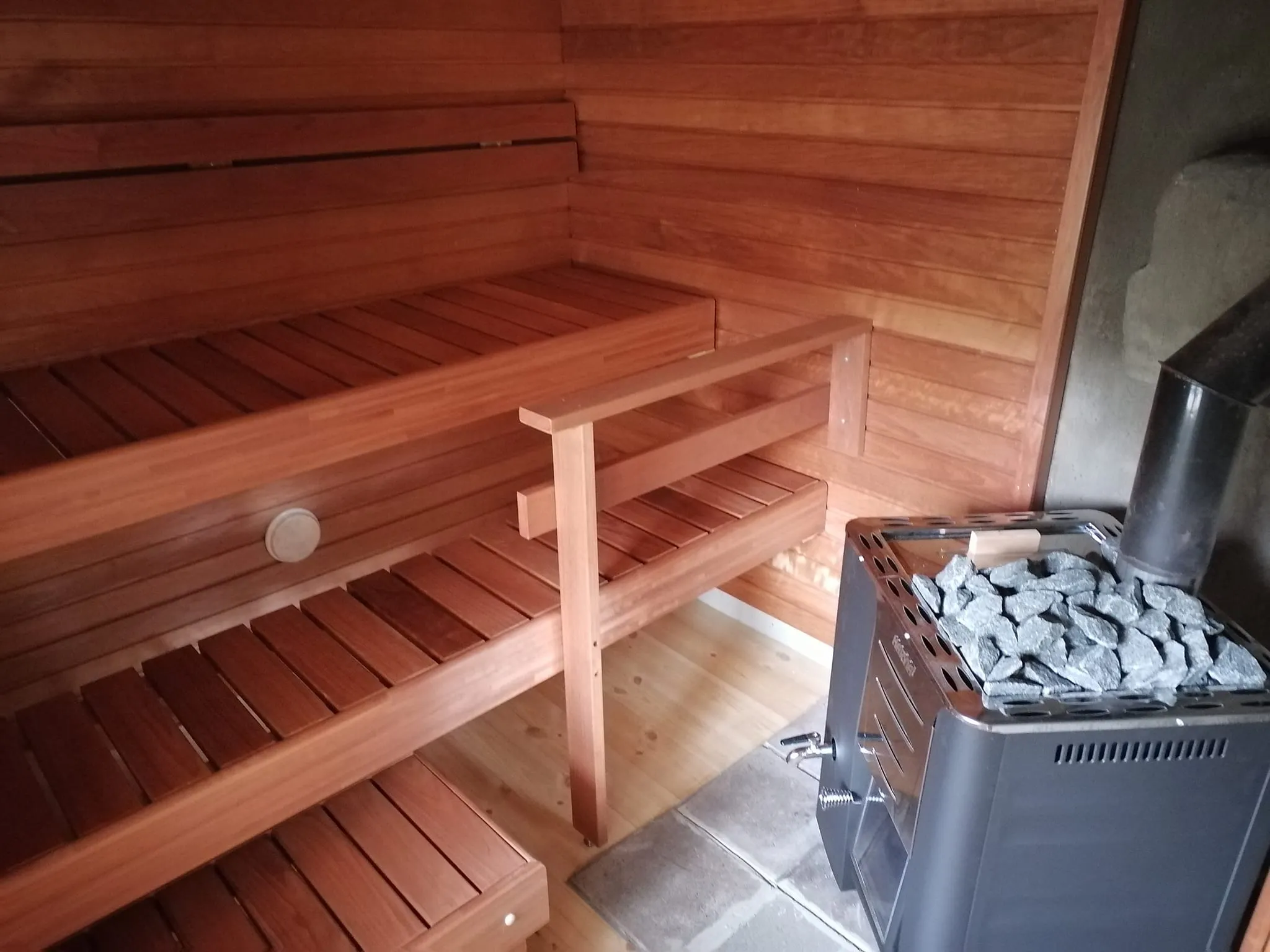 Saunan sisätila, jossa on puupenkit ja kiuas täynnä kiviä, luoden lämpimän ja rentouttavan tunnelman.