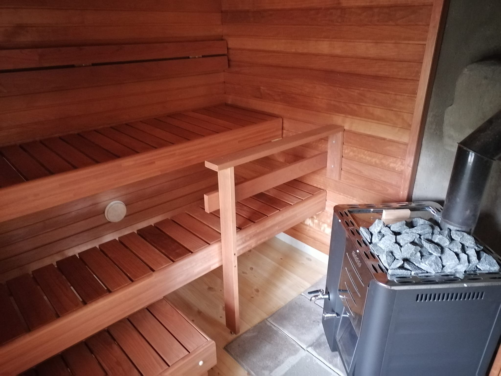 Saunan sisätila, jossa on puupenkit ja kiuas täynnä kiviä, luoden lämpimän ja rentouttavan tunnelman.