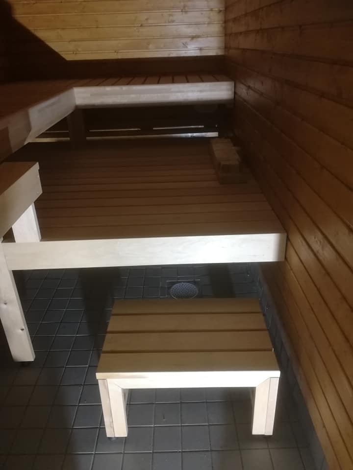 Sauna, jossa on puupaneelit, penkit ja lattiaviemäri, valaistus on lämmin ja tunnelmallinen.