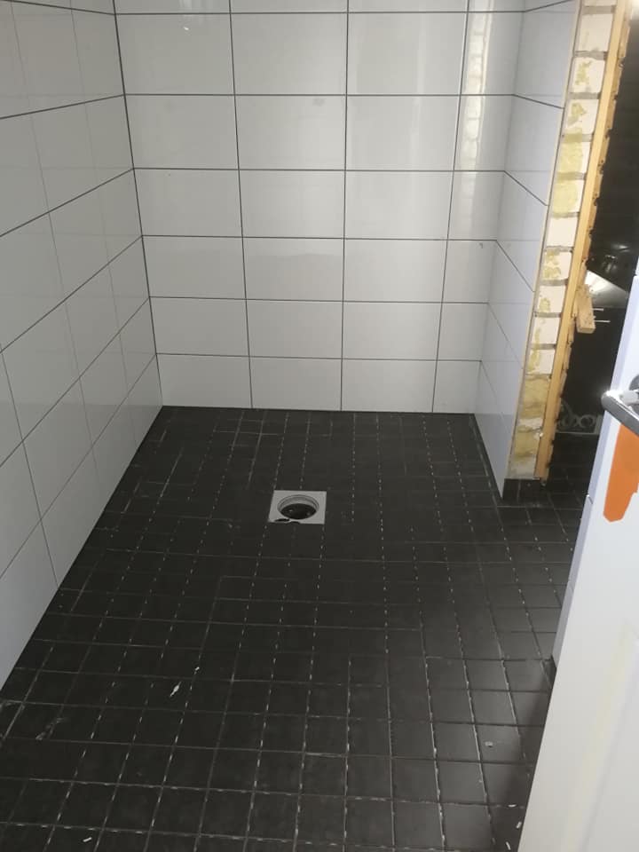 Kuvassa on suihkutila, jossa on valkoiset seinälaatat ja tummat lattialaatat sekä lattiakaivo. Valoisa ja moderni.