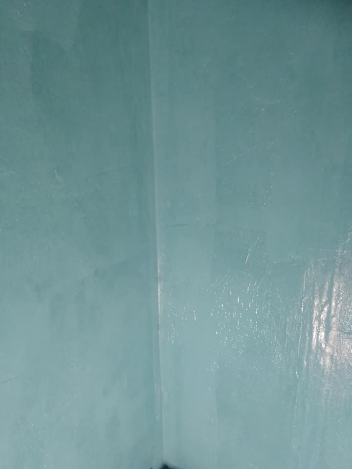 Turkoosi seinä kulmassa, jossa on epätasainen pinta ja heikko valaistus.