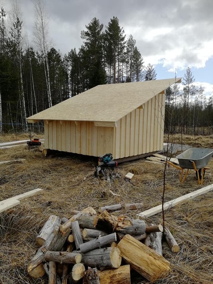 Puinen vaja rakennusvaiheessa, ympärillä puita, taivas pilvinen, maassa puita ja kottikärryt.
