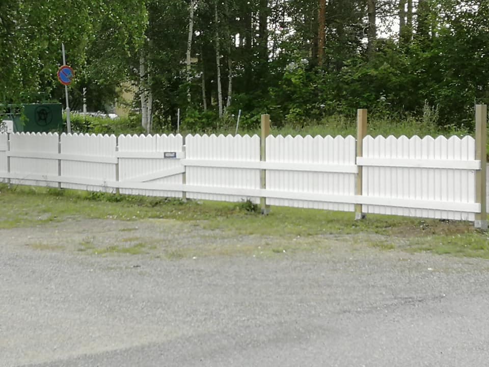 Valkoinen aita reunustaa pihaa, taustalla puita ja liikennemerkki.