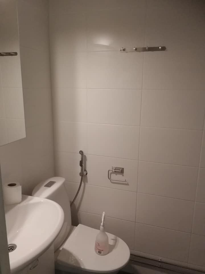 Valkoinen kylpyhuone, jossa on pesuallas, wc-istuin, bidee-suihku ja pyyhekoukku. Valoisa ja yksinkertainen sisustus.