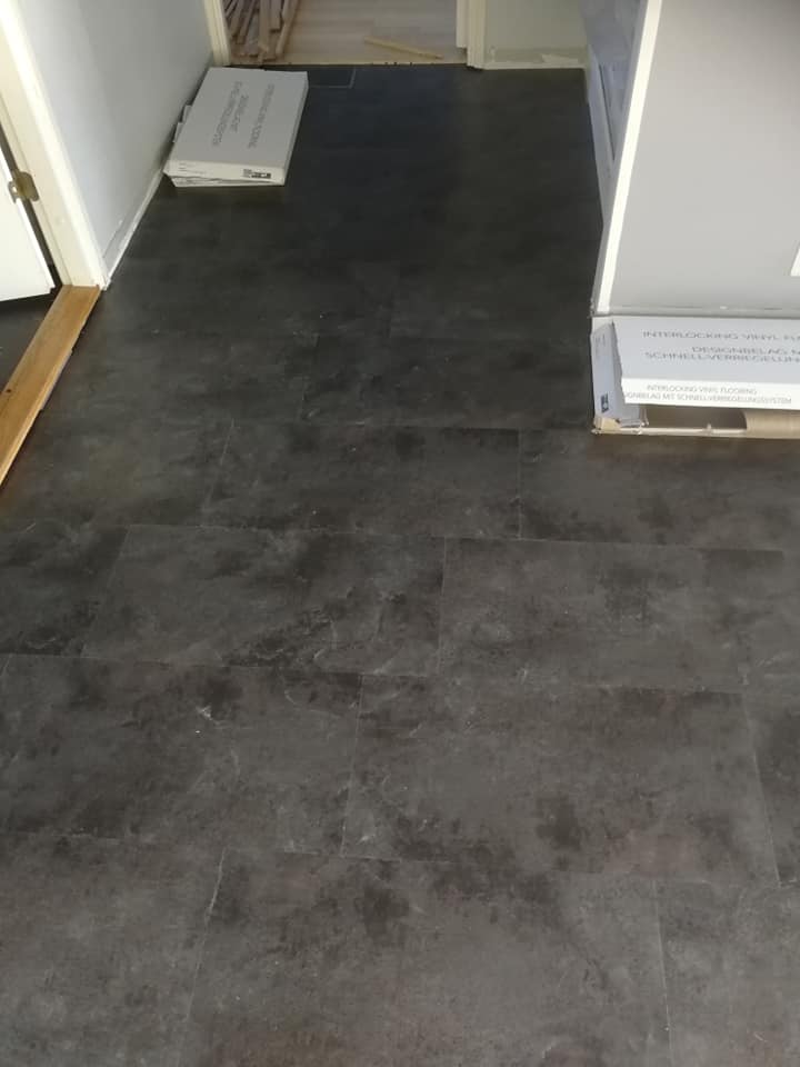 Tummanharmaa vinyylilattialattia, jossa on laatat ja kaksi laatikkoa, jotka on merkitty "INTERLOCKING VINYL FLOORING".